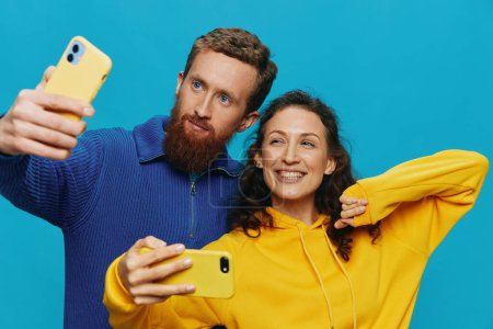 Foto de Mujer y hombre divertida pareja con teléfonos en la mano tomando selfies sonrisa torcida diversión, sobre fondo azul. El concepto de relaciones familiares reales, hablar por teléfono, trabajar en línea. Foto de alta calidad - Imagen libre de derechos