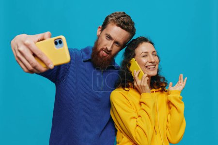 Foto de Mujer y hombre divertida pareja con teléfonos en la mano tomando selfies sonrisa torcida diversión, sobre fondo azul. El concepto de relaciones familiares reales, hablar por teléfono, trabajar en línea. Foto de alta calidad - Imagen libre de derechos
