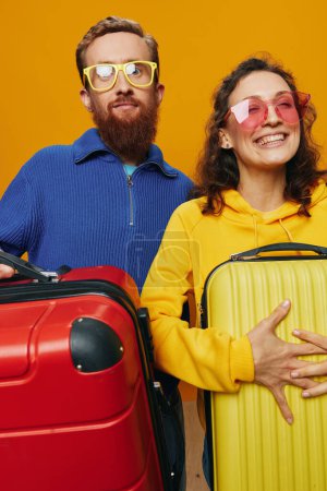 Téléchargez les photos : Femme et homme souriant, valises à la main avec valise jaune et rouge souriant joyeusement et tordu, fond jaune, aller en voyage, voyage de vacances en famille, jeunes mariés. Photo de haute qualité - en image libre de droit