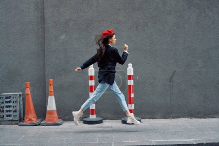 Photo for Fashion woman running down the street in front of the city tourist in stylish clothes with red lips and red beret, travel, cinematic color, retro vintage style. High quality photo - Royalty Free Image