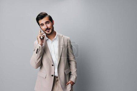 Téléchargez les photos : Homme costume beige portrait app smartphone gris succès personne gars beau téléphone espace sourire homme heureux affaires en ligne attente internet appel copie - en image libre de droit