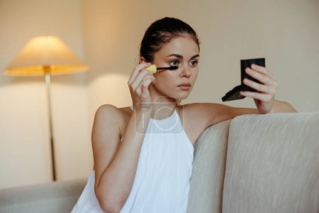 Foto de Una mujer en casa se mira en el espejo y aplicar maquillaje pestañas rímel tinte, concepto de belleza, el cuidado de la piel problema con el acné. Foto de alta calidad - Imagen libre de derechos