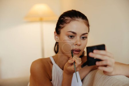 Foto de Una mujer en casa se mira en el espejo y aplica lápiz labial de maquillaje, concepto de belleza, problemas de cuidado de la piel con acné, maquillaje en casa. Foto de alta calidad - Imagen libre de derechos
