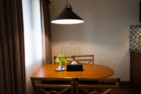 Foto de Interior de la casa oscura con mesa de comedor de madera iluminada por lámpara, luz de la noche para la cena. Foto de alta calidad - Imagen libre de derechos