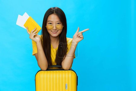 Téléchargez les photos : Femme asiatique voyageant avec une valise jaune et des billets avec passeport à la main, touriste voyageant en avion et en train avec des bagages sur fond bleu. Photo de haute qualité - en image libre de droit