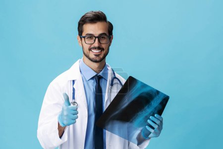 Téléchargez les photos : Médecin homme en manteau blanc chirurgien regarde une radiographie d'un sourire patient sur un fond bleu isolé, espace de copie, espace pour le texte. Photo de haute qualité - en image libre de droit