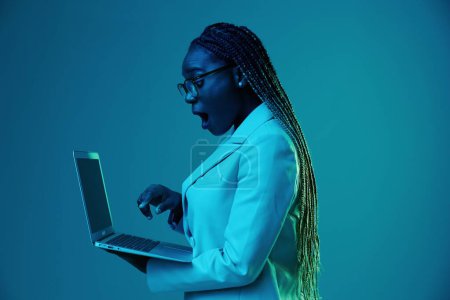 Foto de Mujer africana con portátil en gafas sobre un fondo azul en luz de neón, luz mezclada de color. Ciberseguridad de almacenamiento de datos, hacker, big data. Foto de alta calidad - Imagen libre de derechos