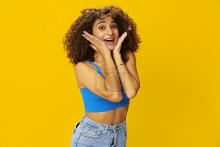 Foto de Mujer con el pelo rizado afro en una camiseta azul. letreros de fondo amarillo con las manos, mirar a la cámara, sonreír con los dientes y la felicidad, espacio de copia. Foto de alta calidad - Imagen libre de derechos