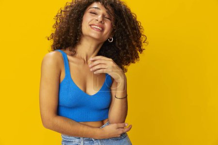 Photo for Woman with curly afro hair in a blue t-shirt on. yellow background signs with her hands, look into the camera, smile with teeth and happiness, copy space. High quality photo - Royalty Free Image