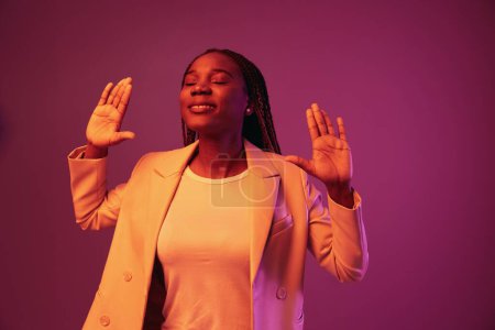 Téléchargez les photos : Femme afro-américaine entreprise sourire danse fête dans la lumière au néon, couleur rose coloré, coloration lumineuse. Photo de haute qualité - en image libre de droit