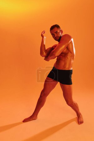 Téléchargez les photos : Homme bodybuilder boxer entraînement musculaire avec torse nu avec abdos posant en studio. Publicité, sport, mode de vie actif, lumière jaune colorée, compétition, concept de défi. . Photo de haute qualité - en image libre de droit