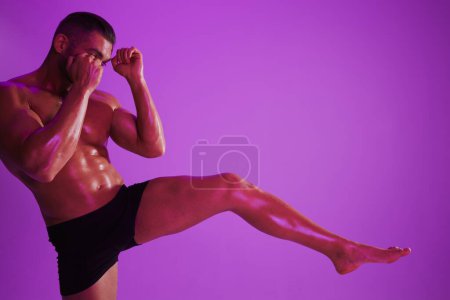 Téléchargez les photos : Homme bodybuilder boxer entraînement musculaire avec torse nu. Publicité, sport, mode de vie actif, lumière violette colorée, compétition, concept de défi. . Photo de haute qualité - en image libre de droit