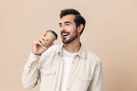 Foto de Retrato de un hombre con estilo con un vaso de café consigo mismo maqueta sobre un fondo beige en una camiseta blanca, estilo de ropa de moda, espacio. Foto de alta calidad - Imagen libre de derechos
