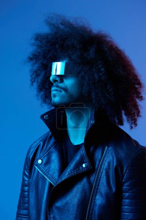 Photo for Portrait of fashion man with curly hair with stylish glasses on blue background multinational, colored light, black leather jacket trend, modern concept. High quality photo - Royalty Free Image