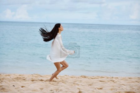 Téléchargez les photos : Femme sportive court le long de la plage en vêtements d'été sur le sable dans un débardeur jaune et short en jean chemise blanche volant cheveux vue sur l'océan, vacances à la plage et Voyage. Photo de haute qualité - en image libre de droit