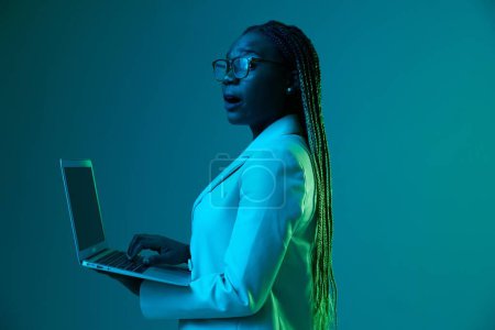 Photo for African African woman with laptop in glasses on a blue background in neon light, color mixed light. Data storage cyber security, hacker, big data. High quality photo - Royalty Free Image