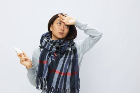 Foto de Mujer asiática cogida de la mano en el resfriado de la gripe de la cabeza dolorida con la nariz congestionada que sostiene la alergia y el aerosol nasal del virus con dolor de garganta en fondo blanco. Foto de alta calidad - Imagen libre de derechos