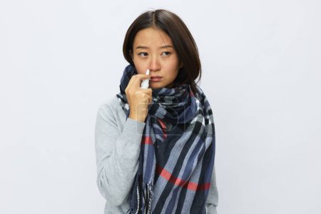 Foto de La mujer asiática resfriada de gripe con nariz tapada sostiene el aerosol nasal y rocía el aerosol nasal para alergias y el virus covid 19 con dolor de garganta sobre fondo blanco. Foto de alta calidad - Imagen libre de derechos