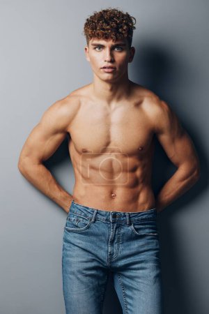 Téléchargez les photos : Homme jeune musclé bicep gris fond sexy corps debout jeans sourire sain athlète sport mâle soins - en image libre de droit