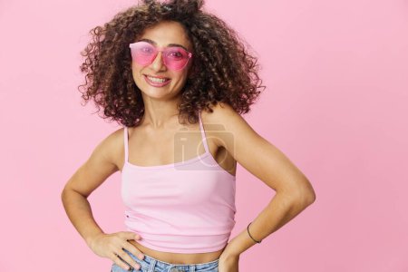 Téléchargez les photos : Happy woman afro boucles cheveux danse sur un fond rose en t-shirt rose d'été jeans et lunettes, ambiance d'été, espace de copie. Photo de haute qualité - en image libre de droit