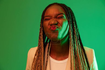 Foto de Mujer afroamericana retrato negocio sonrisa sobre fondo verde en luz de neón, color mezclado luz, colores brillantes. Belleza mujer afroamericana con coletas emociones. Foto de alta calidad - Imagen libre de derechos