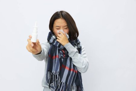 Foto de La mujer asiática resfriada de gripe con nariz tapada sostiene el aerosol nasal de alergia con dolor de garganta sobre fondo blanco. Foto de alta calidad - Imagen libre de derechos