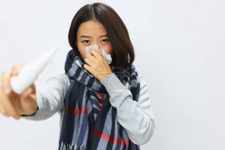 Foto de La mujer asiática resfriada de gripe con nariz tapada sostiene los espectáculos de aerosol nasal en la cámara para alergias con dolor de garganta en el fondo blanco. Foto de alta calidad - Imagen libre de derechos