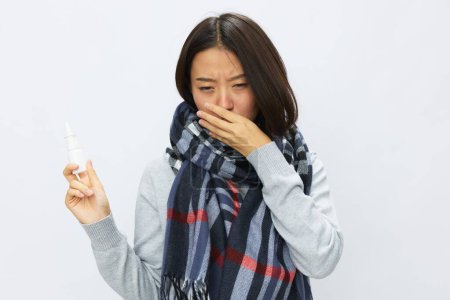 Foto de La mujer asiática resfriada de gripe con nariz tapada sostiene los espectáculos de aerosol nasal en la cámara para alergias con dolor de garganta en el fondo blanco. Foto de alta calidad - Imagen libre de derechos