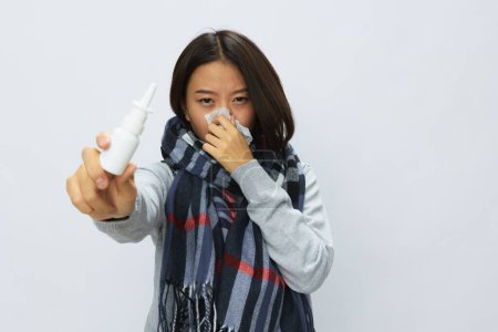 Téléchargez les photos : Femme asiatique grippe froid avec nez bouché tient pulvérisation nasale allergie avec mal de gorge en écharpe à carreaux sur fond blanc. Photo de haute qualité - en image libre de droit