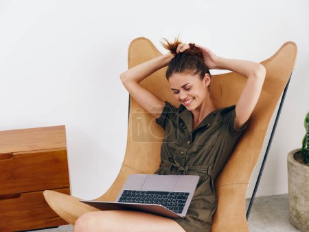 Téléchargez les photos : Femme assise sur une chaise avec un ordinateur portable à la maison beau sourire et détente, style de vie scandinave intérieur élégant moderne, espace de copie. Photo de haute qualité - en image libre de droit
