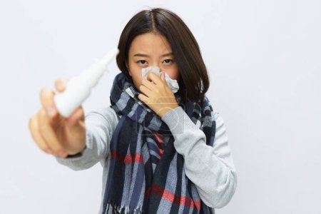 Téléchargez les photos : Femme asiatique grippe froid avec nez bouché tient pulvérisation nasale montre à la caméra pour les allergies avec mal de gorge sur fond blanc. Photo de haute qualité - en image libre de droit