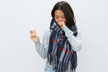 Téléchargez les photos : Femme asiatique grippe froide avec nez bouché tenant pulvérisation d'allergie et mal de gorge avec mal de gorge sur fond blanc. Photo de haute qualité - en image libre de droit