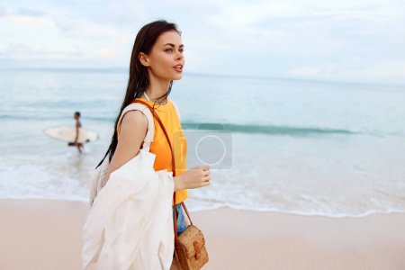 Téléchargez les photos : Jeune femme avec un sac à dos marche sur la plage, vacances d'été sur une île au bord de l'océan à Bali. Photo de haute qualité - en image libre de droit