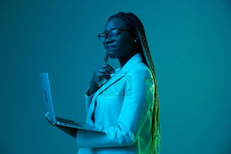 Photo for African African woman with laptop in glasses on a blue background in neon light, color mixed light. Data storage cyber security, hacker, big data. High quality photo - Royalty Free Image