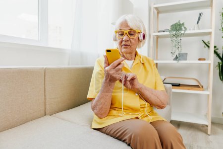 Foto de Mujer de edad avanzada feliz mirando en su videollamada del teléfono con la sonrisa de los auriculares, tecnología para la comunicación, interior moderno brillante, estilo de vida comunicación en línea. Foto de alta calidad - Imagen libre de derechos