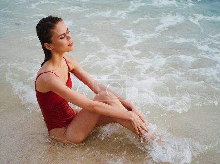Téléchargez les photos : Une femme en maillot de bain rouge est assise sur le sable avec un beau bronzage et regarde l'océan sous les tropiques sur Bali Island Beach. Photo de haute qualité - en image libre de droit