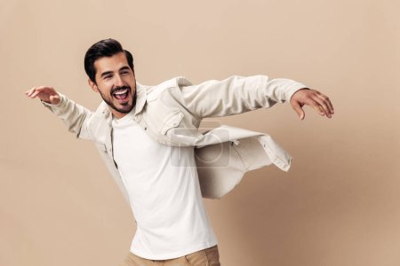 Photo for Stylish man smile runs and jumps on a beige background in a white t-shirt and business jacket, flying clothes hero, fashionable clothing style, copy space, space for text. High quality photo - Royalty Free Image
