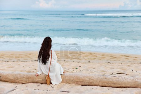 Téléchargez les photos : Une femme aux longs cheveux mouillés après avoir nagé s'assoit sur le sable dos à la caméra et regarde le coucher de soleil sur l'île de Bali. Photo de haute qualité - en image libre de droit