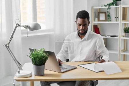 Foto de Hombre americano tecnología en línea freelancer interior oficina casa buscando educación estudiante portátil trabajo chat escritorio ordenador africano en blanco lugar de trabajo internet carrera espacio de trabajo - Imagen libre de derechos