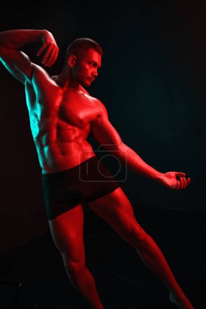 Téléchargez les photos : Homme bodybuilder athlète avec torse nu pose de mode sur fond noir isolé avec lumière colorée néon rouge et vert. Le concept d'un sport sain du corps masculin. Photo de haute qualité - en image libre de droit
