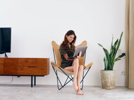 Photo for Female student study sits on a chair with a laptop work at home smile and relax, modern stylish interior Scandinavian lifestyle, copy space. High quality photo - Royalty Free Image