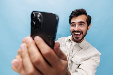 Photo for Portrait of a stylish man brunette smile and open mouth looks at the phone blogger with a beard, on a blue background in a white T-shirt and jeans, copy space. High quality photo - Royalty Free Image