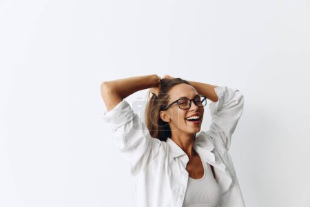 Téléchargez les photos : Femme heureuse s'amuser à la maison dans un haut blanc et chemise blanche avec des lunettes contre un mur blanc, style de vie. Photo de haute qualité - en image libre de droit