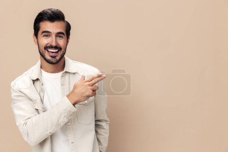 Foto de Retrato de un hombre elegante sonrisa con dientes y sorpresa levantó las manos sobre un fondo beige en una camiseta blanca, estilo de ropa de moda, espacio de copia, espacio para el texto. Foto de alta calidad - Imagen libre de derechos
