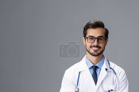 Téléchargez les photos : Médecin masculin en manteau blanc et lunettes pour la vision et un stéthoscope regarde le sourire de la caméra avec dentiste dents sur un fond gris isolé, espace de copie, espace pour le texte, la santé. Photo de haute qualité - en image libre de droit