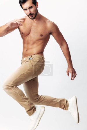 Photo for Male fashion model with a naked torso and abs packs jumping on a white isolated background, fashionable clothing style, copy space, space for text. High quality photo - Royalty Free Image