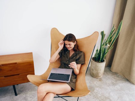 Téléchargez les photos : Femme assise sur une chaise avec un ordinateur portable à la maison beau sourire et détente, style de vie scandinave intérieur élégant moderne, espace de copie. Photo de haute qualité - en image libre de droit