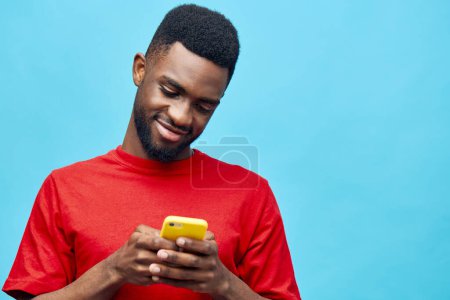 Foto de Mano hombre modelo emocionado sonrisa africano joven aplicación tecnología retrato móvil pantalla chico teléfono colorido masculino azul negro fondo feliz estudio aplicación - Imagen libre de derechos
