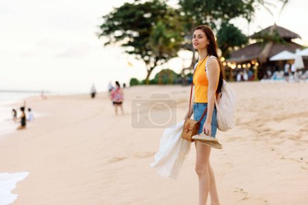 Foto de Una mujer joven después de nadar en el océano con una mochila con ropa mojada camina a lo largo de la playa, vacaciones de verano en una isla cerca del océano en Bali. Foto de alta calidad - Imagen libre de derechos