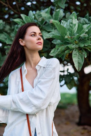 Téléchargez les photos : Portrait de beauté d'une femme aux cheveux mouillés en chemise blanche près des feuilles d'un arbre tropical, peau bronzée beauté et santé. Photo de haute qualité - en image libre de droit
